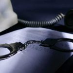 Smart Ring CEO Convicted in $2 Million Scheme Handcuffs on a document beside a coiled telephone handset