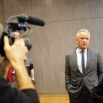 HHS Secy to Address Children’s Health Defense Man in a gray suit speaks to a reporter during an interview