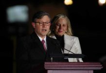 Man speaking at a podium with a woman standing behind him