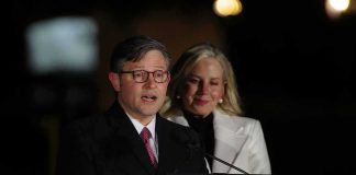 Man speaking at a podium with a woman standing behind him