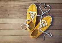 Yellow canvas sneakers with laces forming a heart on wooden floor