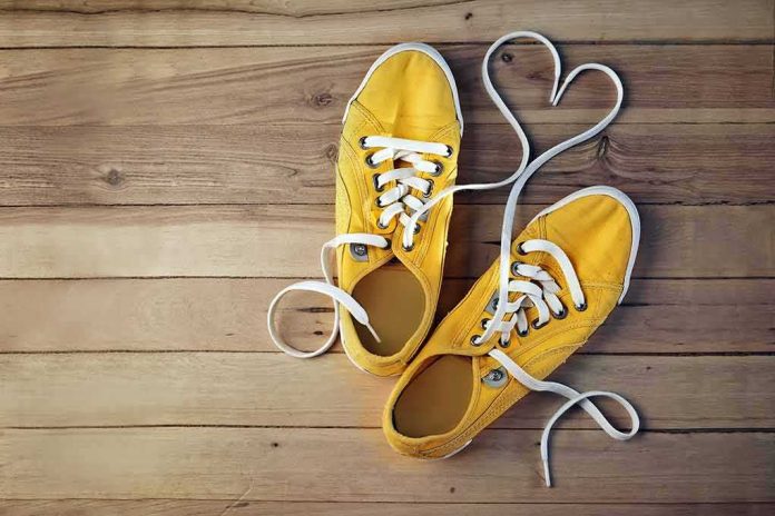 Yellow canvas sneakers with laces forming a heart on wooden floor