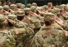 Soldiers in camouflage uniforms salute in formation