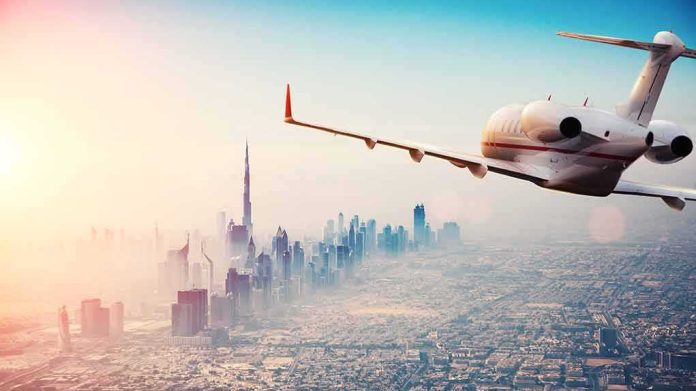 shutterstock_1164679735 Private jet flying over a modern city skyline at sunrise
