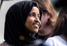 Ilhan Omar smiling in a black hijab at an outdoor event