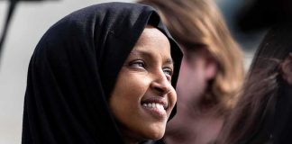 Ilhan Omar smiling in a black hijab at an outdoor event