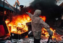 Hooded person throws object near street fire