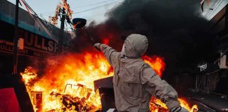 Hooded person throws object near street fire