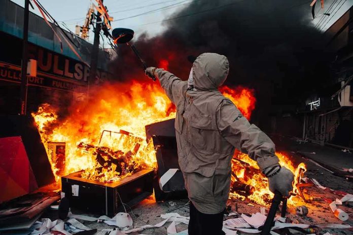 shutterstock_1540874357 Hooded person throws object near street fire