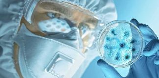 Scientist in protective gear examining a petri dish