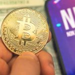 Bitcoin coin held next to a smartphone displaying NFT screen