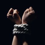 Hands bound with white rope against dark background