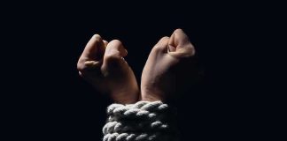 Hands bound with white rope against dark background