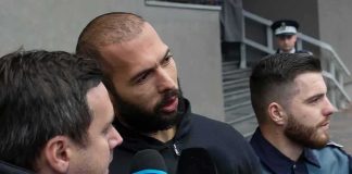 Man speaking to reporters with microphones outside a building