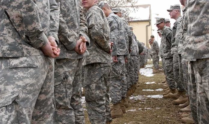 Soldiers in camouflage uniforms stand in two facing rows outdoors